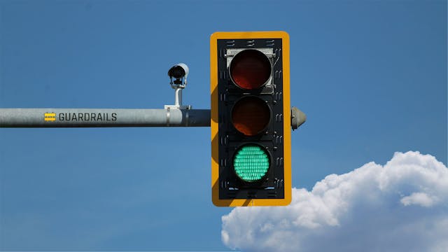 Green traffic light against blue sky with large cloud.